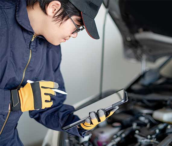 NCC auto mechanic holding digital tablet checking car engine under the hood in auto service garage