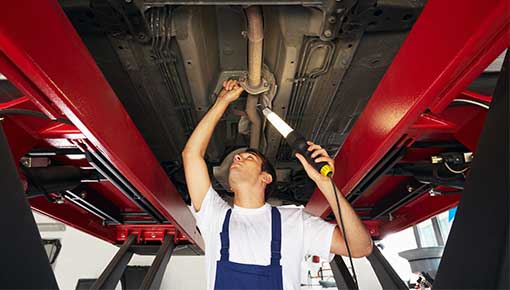 NCC mechanic standing under car engine and holding lamp
